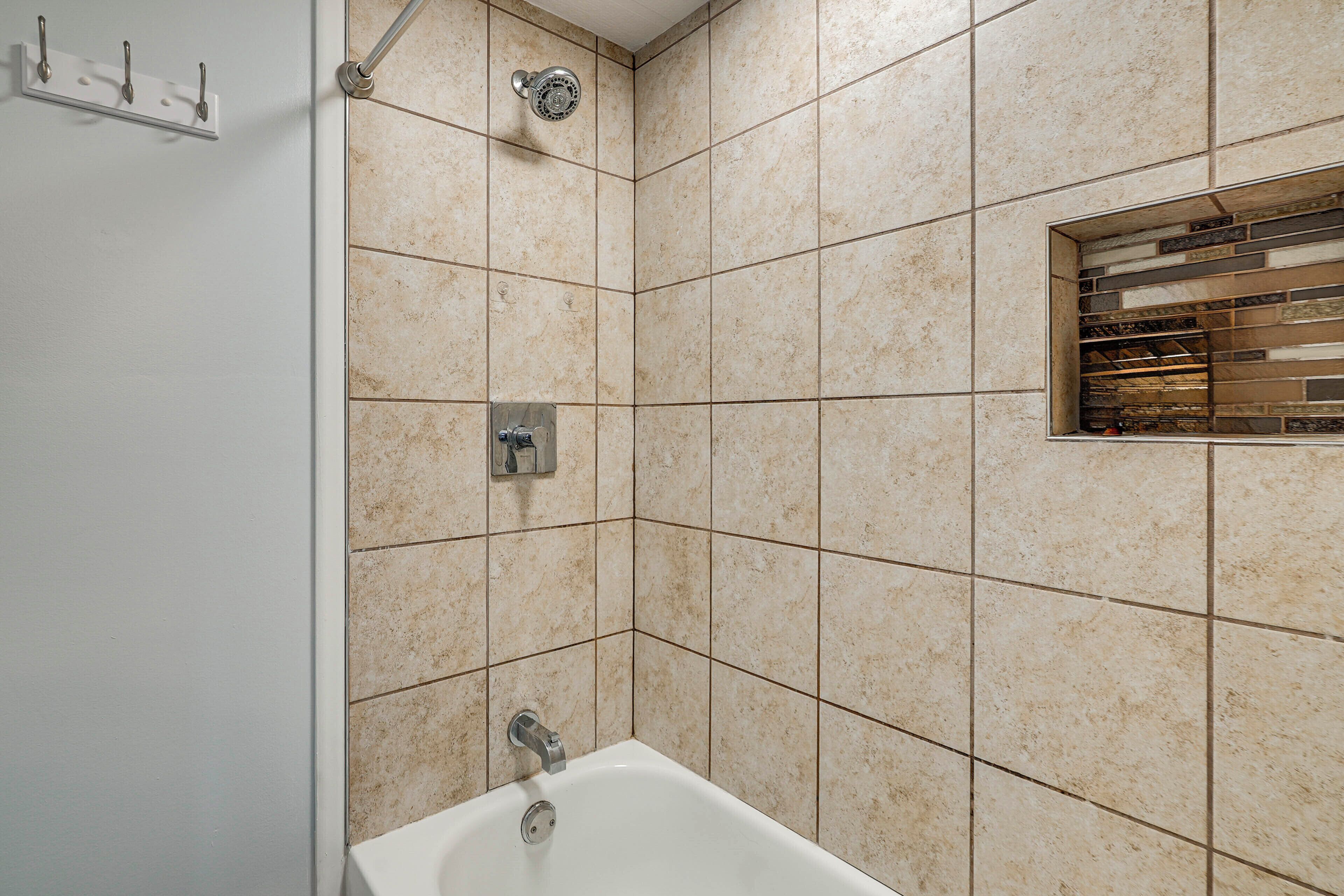 A bathroom with a white bathtub, a showerhead, and a small window with a metal grate.