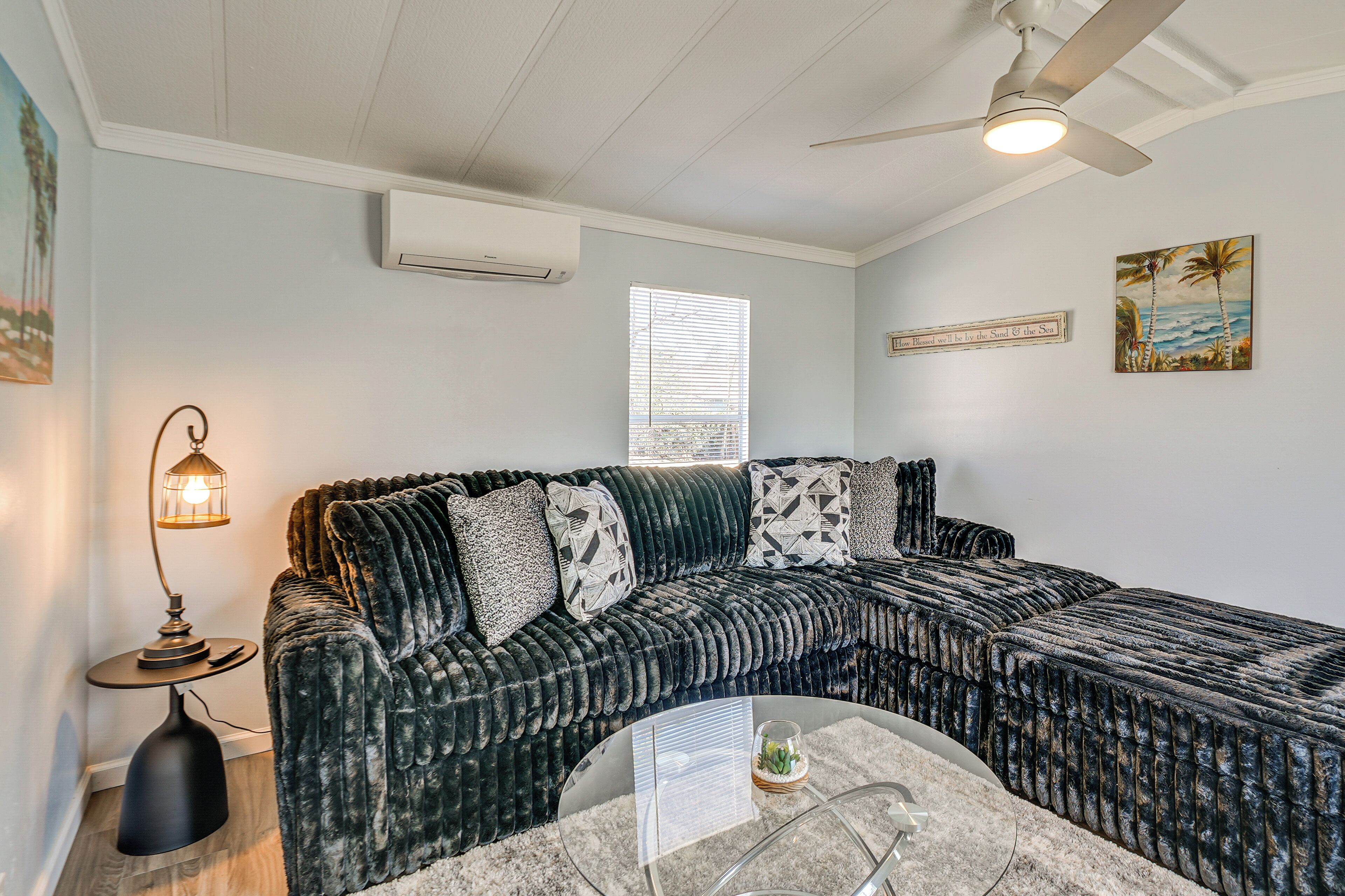 A cozy living room with a sectional sofa, a glass coffee table, a ceiling fan, and a painting on the wall.