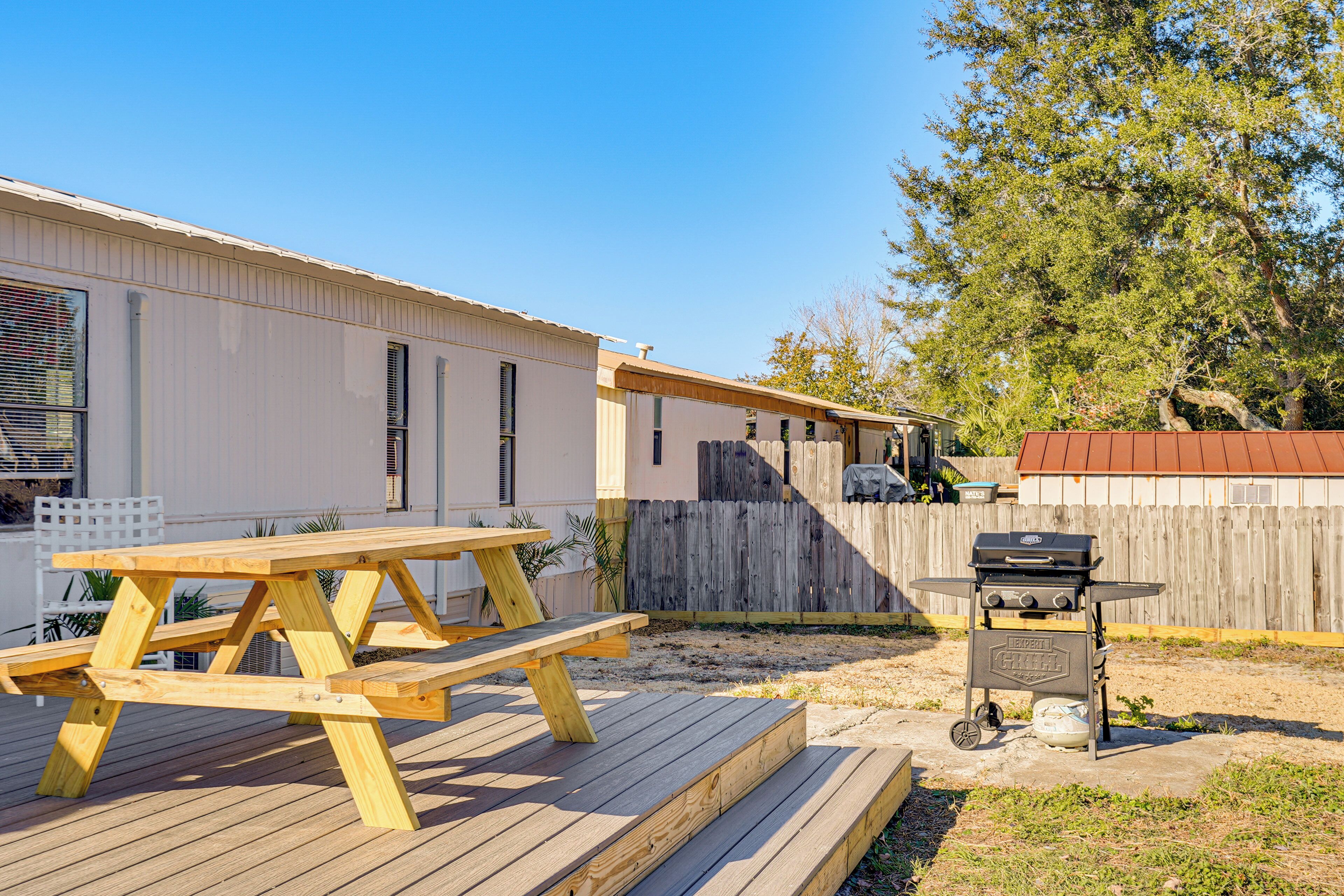 A wooden deck with a picnic table, a barbecue grill, and a fenced yard.