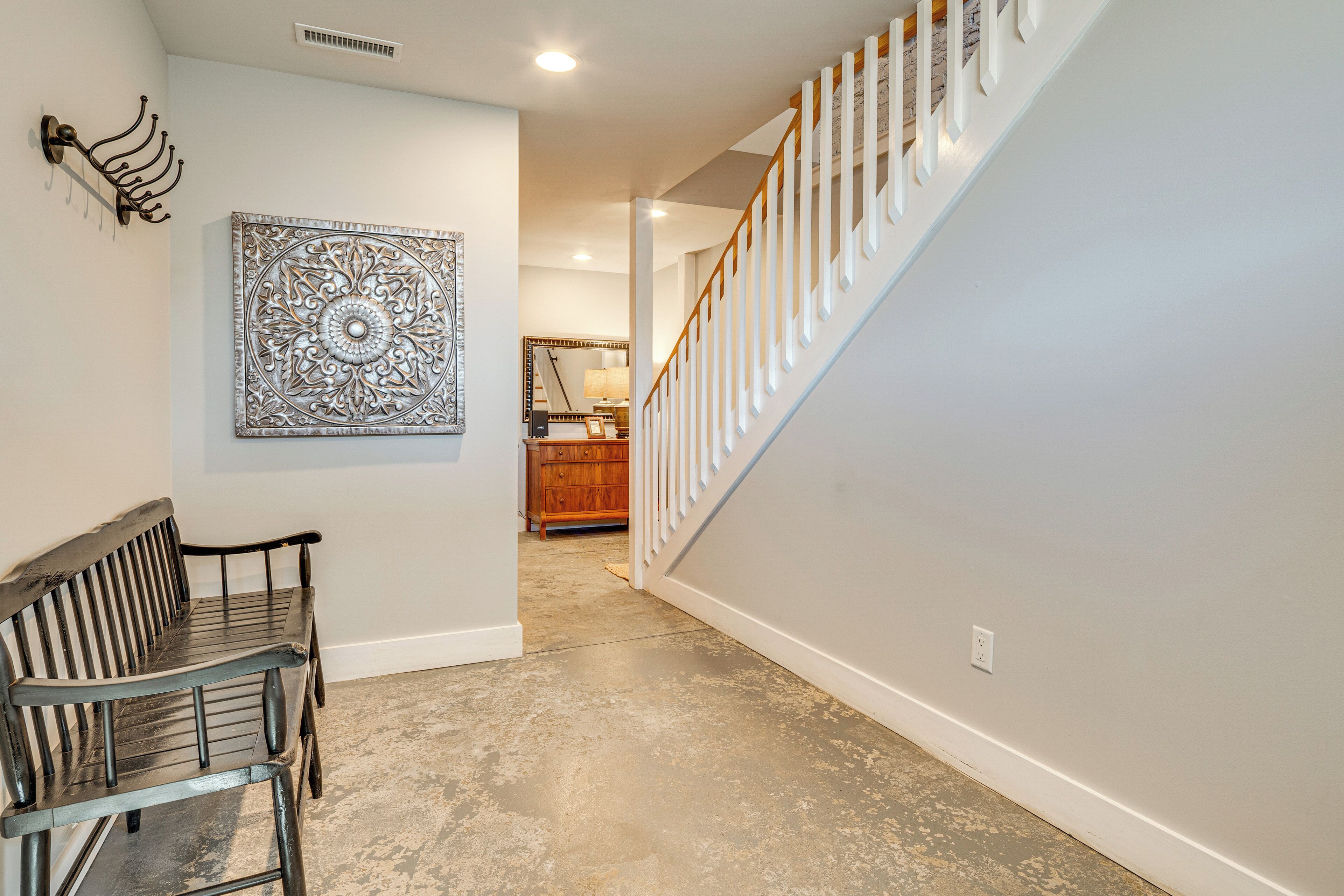 A hallway with a bench, a decorative wall piece, and a staircase.