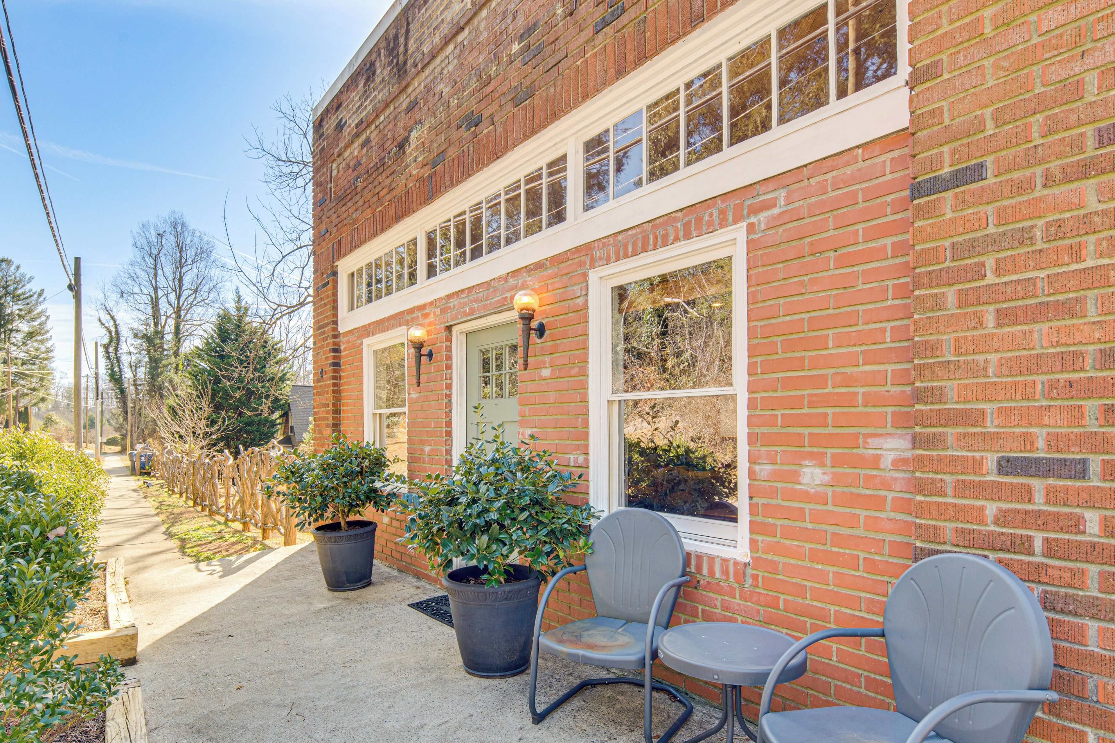 Een bakstenen gebouw met een veranda, twee plantenpotten en twee stoelen.