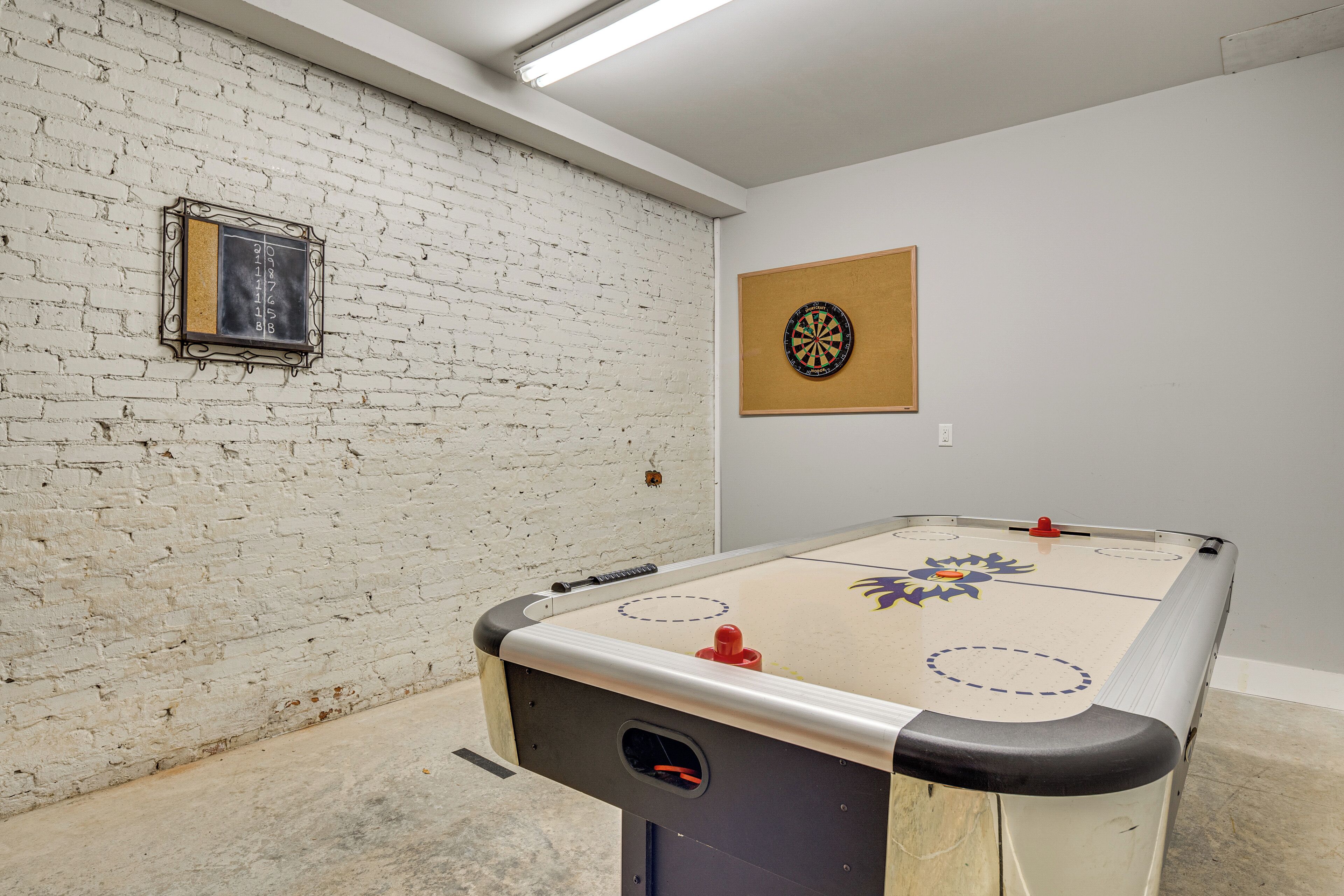 A room with a foosball table, a dartboard, and a brick wall.
