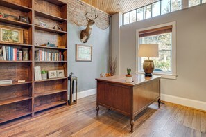 A room with a wooden desk, bookshelves, a mounted deer head, a lamp, and a window with a view of trees. - Private Hot Tub, Steps to Main St: Saluda Retreat (Saluda)