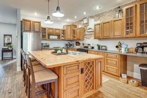 A spacious kitchen with wooden cabinets, a stainless steel refrigerator, and a large island with bar stools. - Private Hot Tub, Steps to Main St: Saluda Retreat (Saluda)