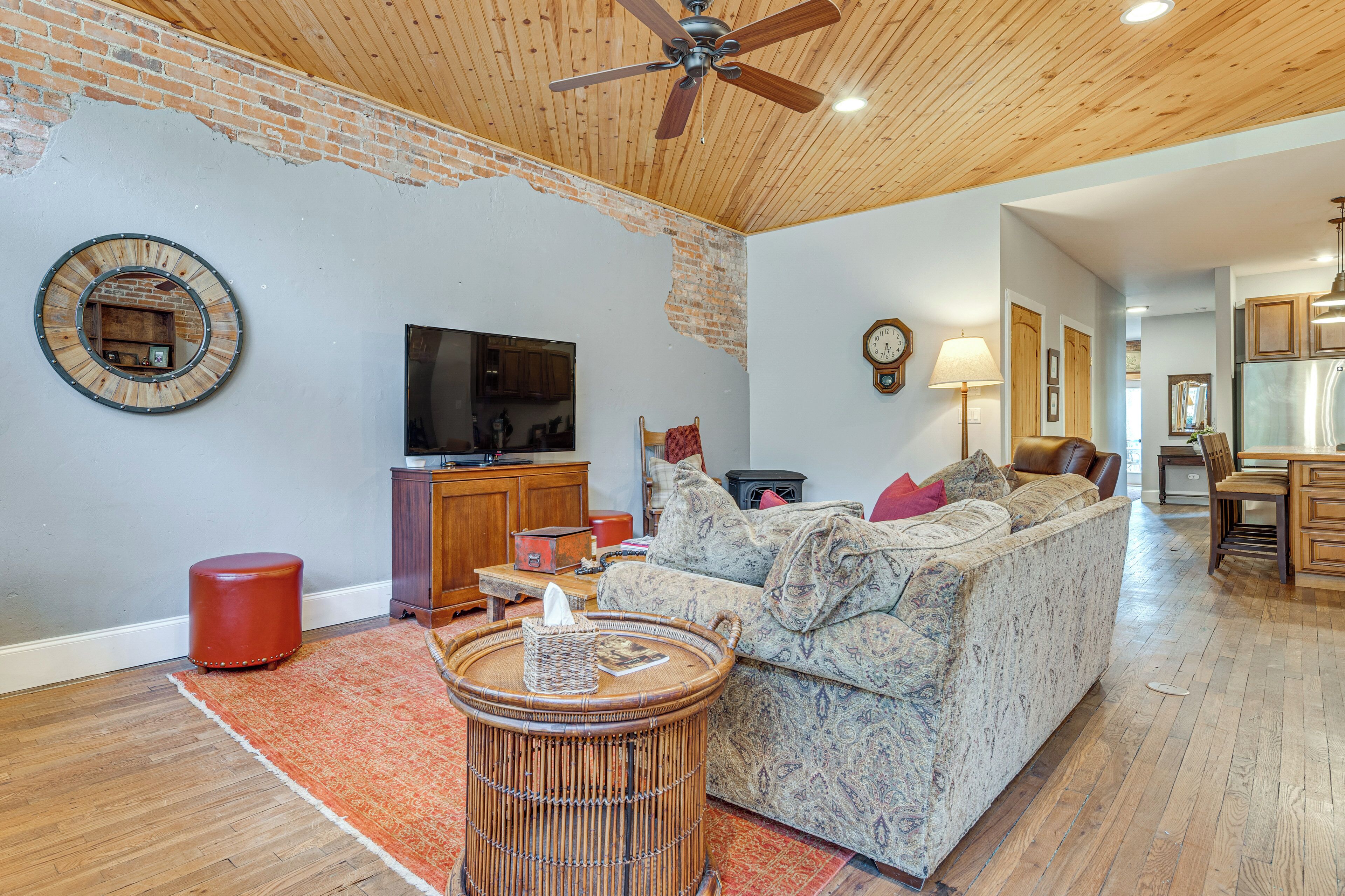 A living room with a brick wall, wooden ceiling, a round table, a sofa, and a television.