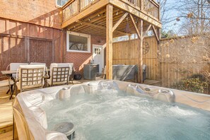 A hot tub with a wooden deck and chairs, a brick wall, and a wooden fence. - Private Hot Tub, Steps to Main St: Saluda Retreat (Saluda)