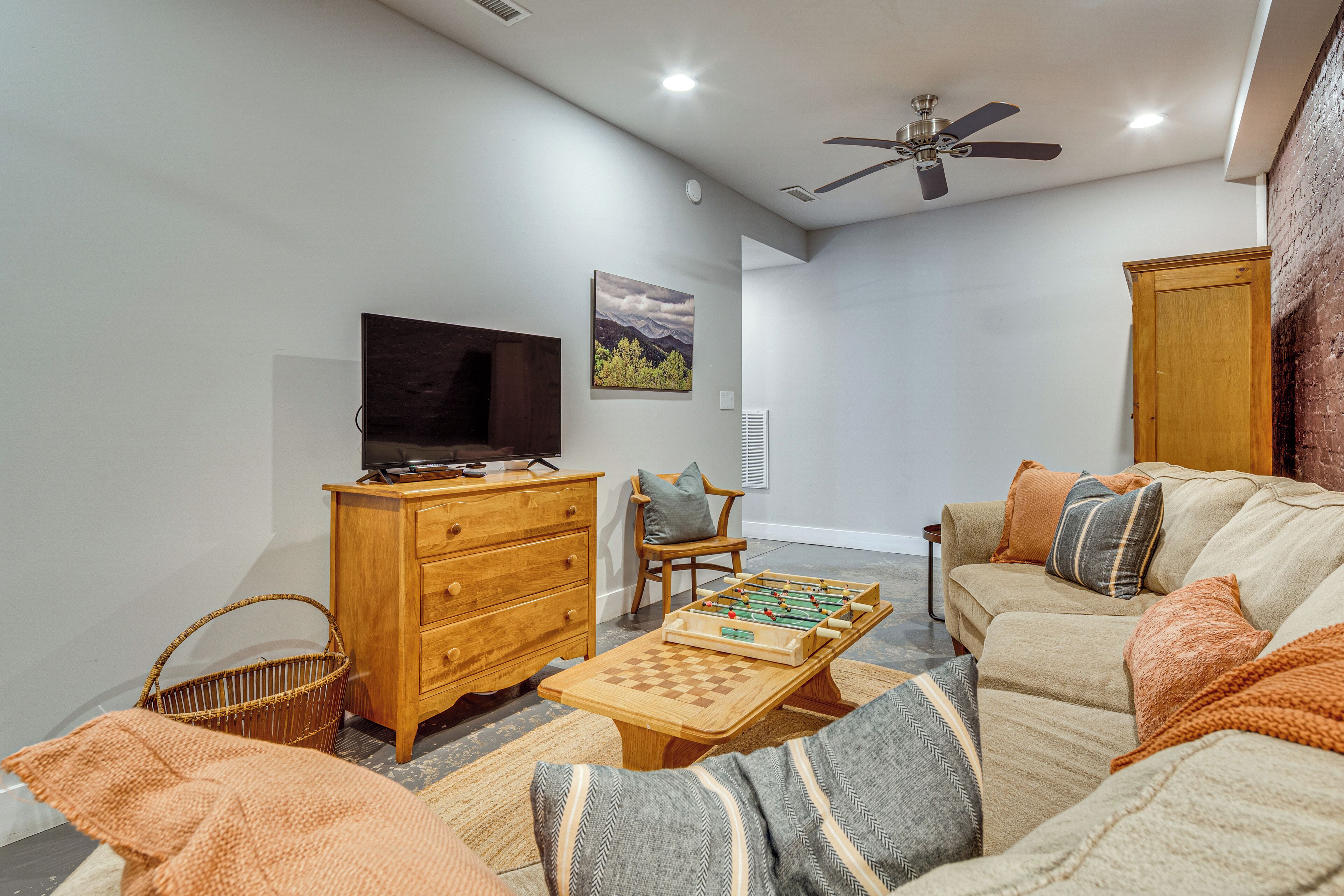 A living room with a sofa, a television, a wooden dresser, a foosball table, and a ceiling fan.