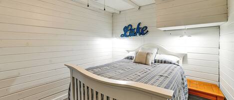 A bedroom with a white bed, a wooden nightstand, a ceiling fan, and a wall-mounted sign.
