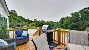 A deck with outdoor furniture, a grill, and a view of a forested area.