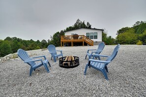 A deck with four blue chairs and a fire pit in the center, surrounded by gravel. - Cozy Hillside Retreat Near Dale Hollow Lake! (Burkesville)