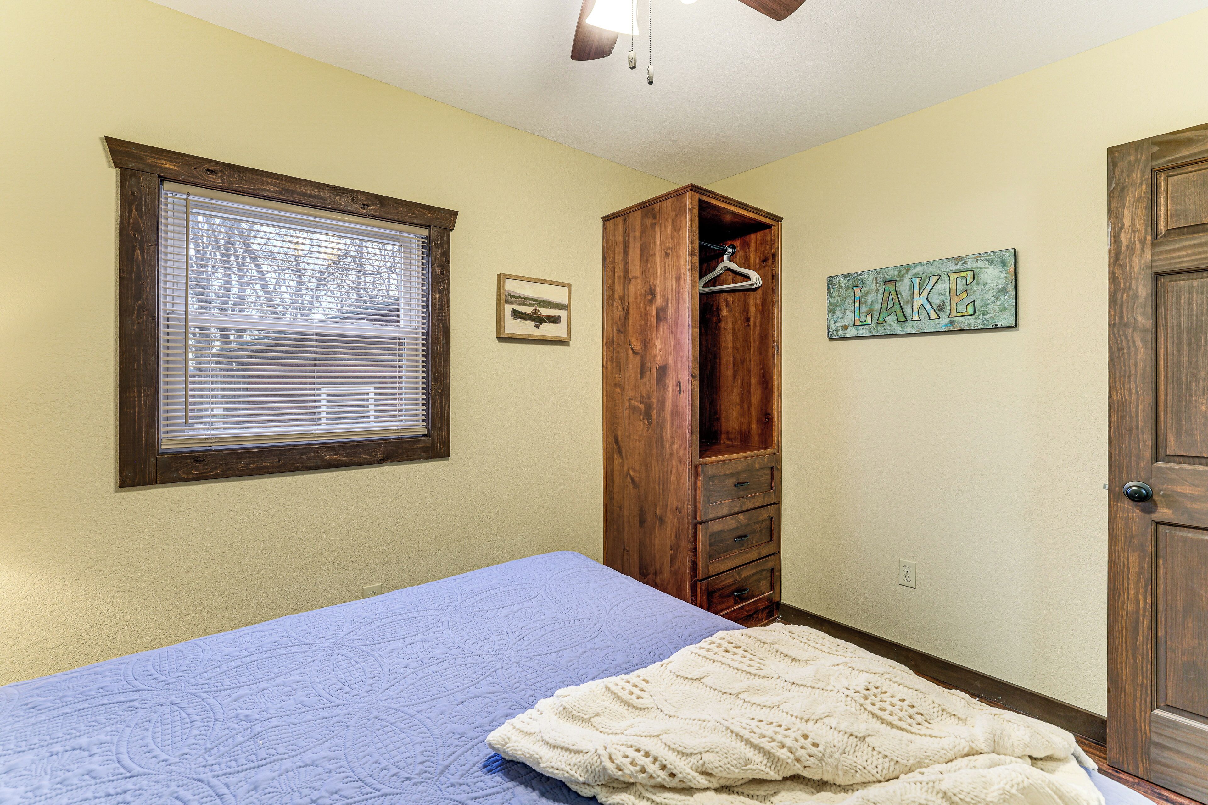 A bedroom with a bed, a wooden wardrobe, a window with blinds, and a wall-mounted sign.