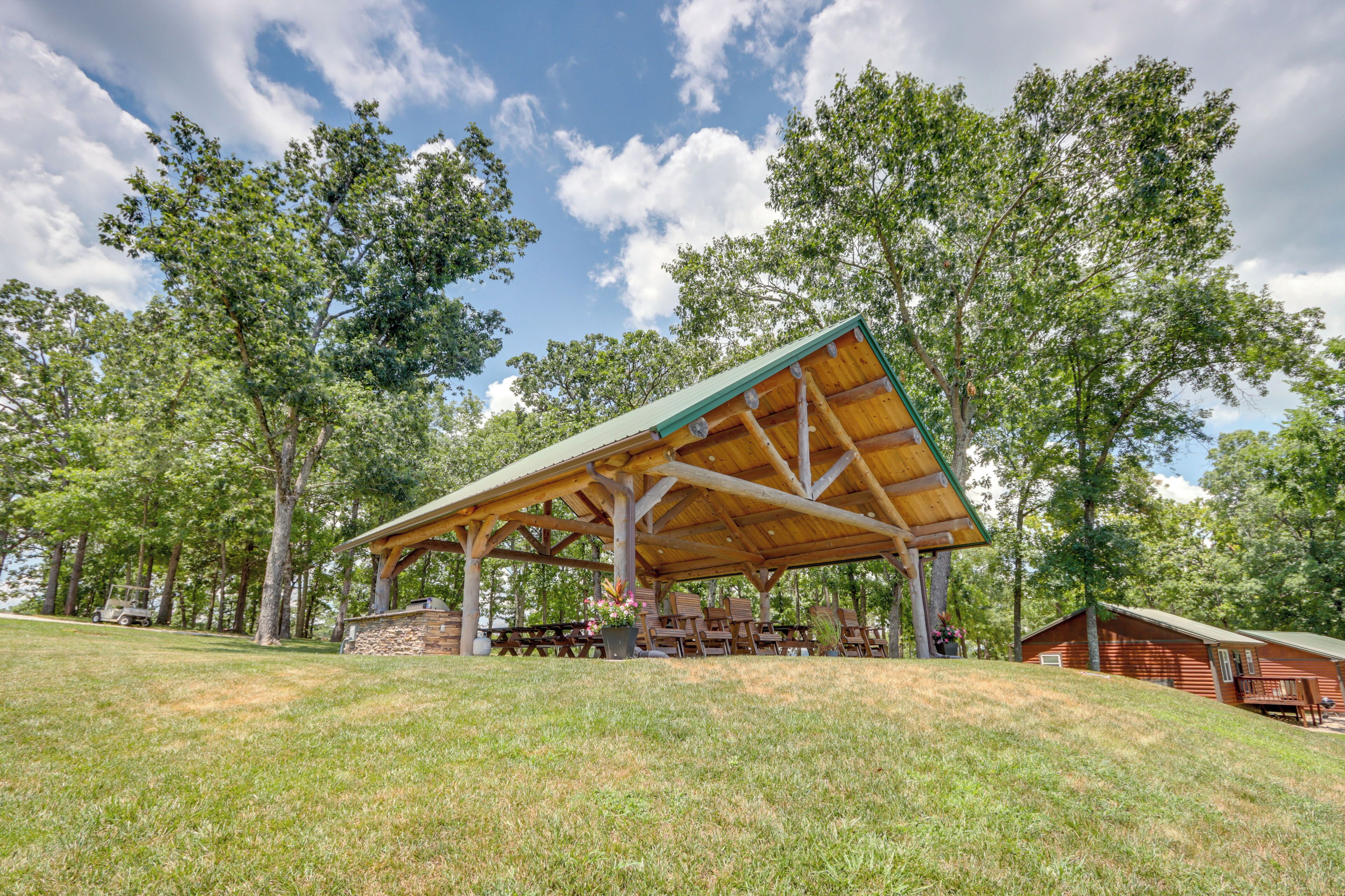 Un pavillon abrité avec des tables de pique-nique, un mur en pierre et un chalet situé dans une zone boisée.
