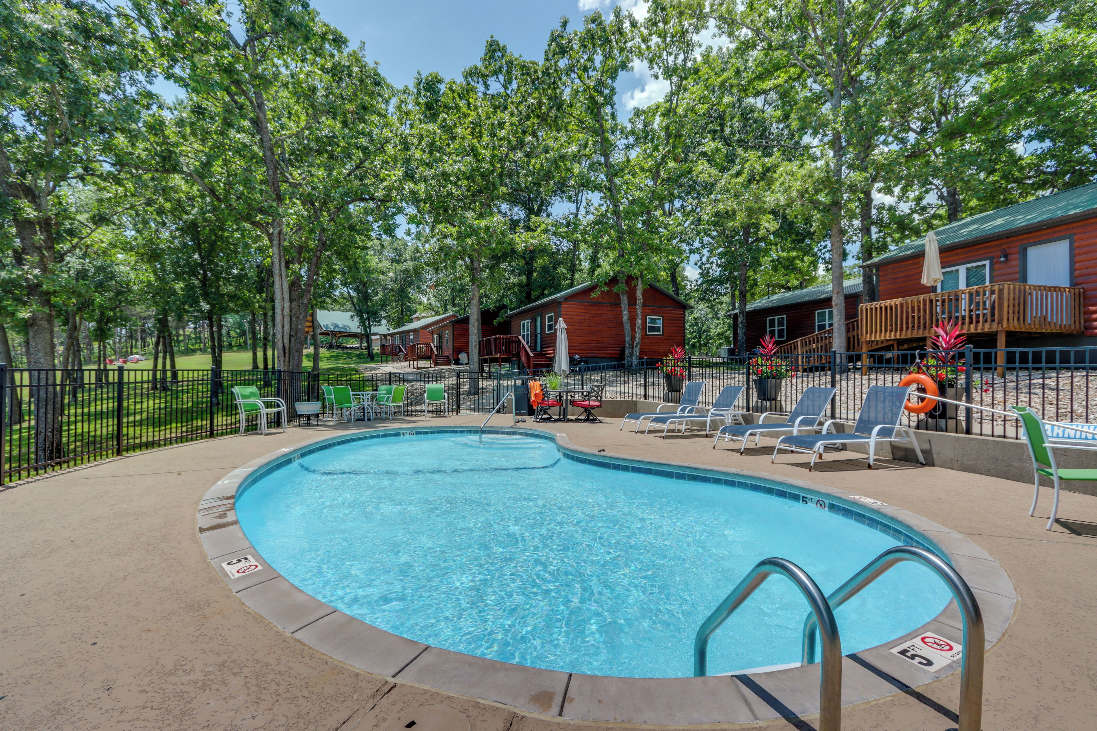A swimming pool with lounge chairs and a deck area, surrounded by trees and cabins.