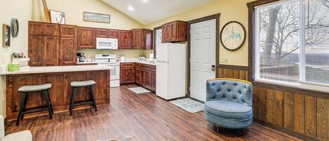 Una cocina con armarios de madera, un refrigerador blanco y una zona de comedor con un taburete alto y una silla.