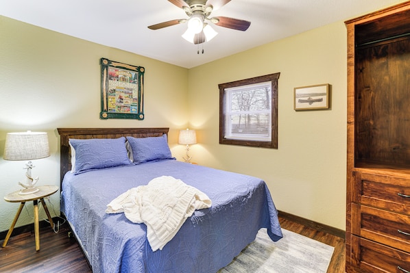 A bedroom with a bed, two bedside lamps, a ceiling fan, a framed picture on the wall, and a wooden cabinet. - Stunning Views! Table Rock Lake Cabin Near Marina (Shell Knob)