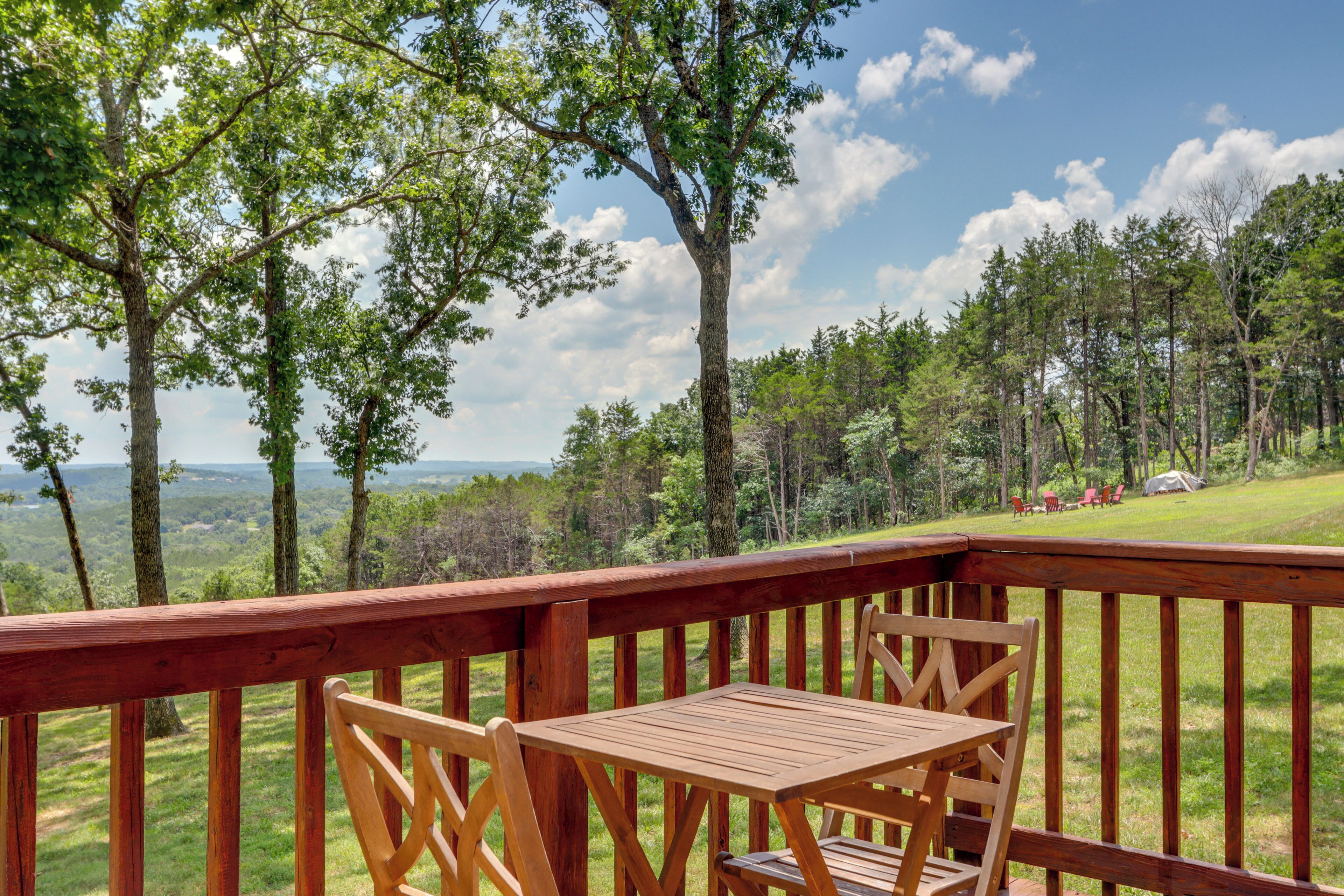 A wooden deck with a table and chairs, overlooking a forested landscape.