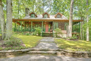 A rustic cabin with a stone chimney, wooden deck, and a stone pathway leading to the entrance. - Vintage Home Nestled in the Woods of Smoky Mtns (Marble)