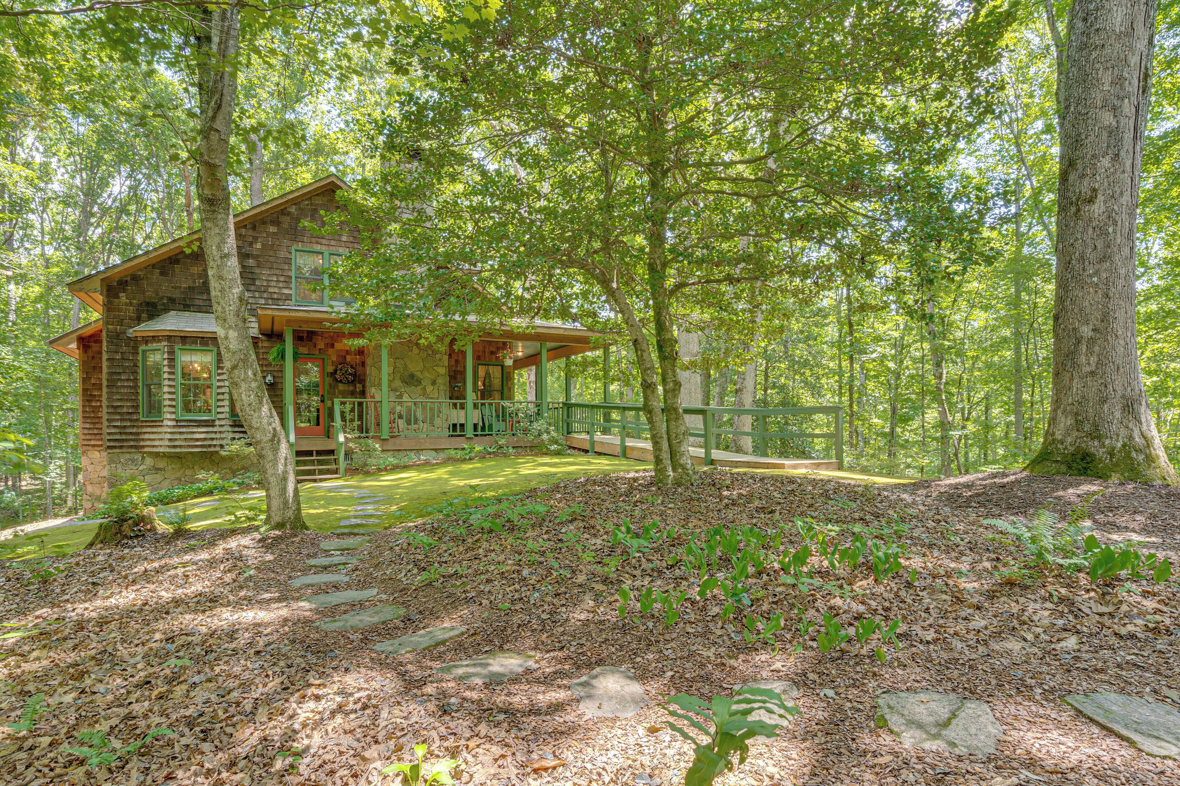 A cabin with a stone foundation and wooden siding, surrounded by a forest with a stone pathway leading to the entrance.