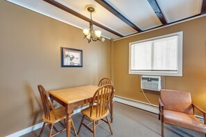 A dining area with a wooden table and chairs, a chandelier, a framed picture on the wall, and a window with blinds. - Walk to Lifts! Skier's Black Mountain Base Camp (Jackson)