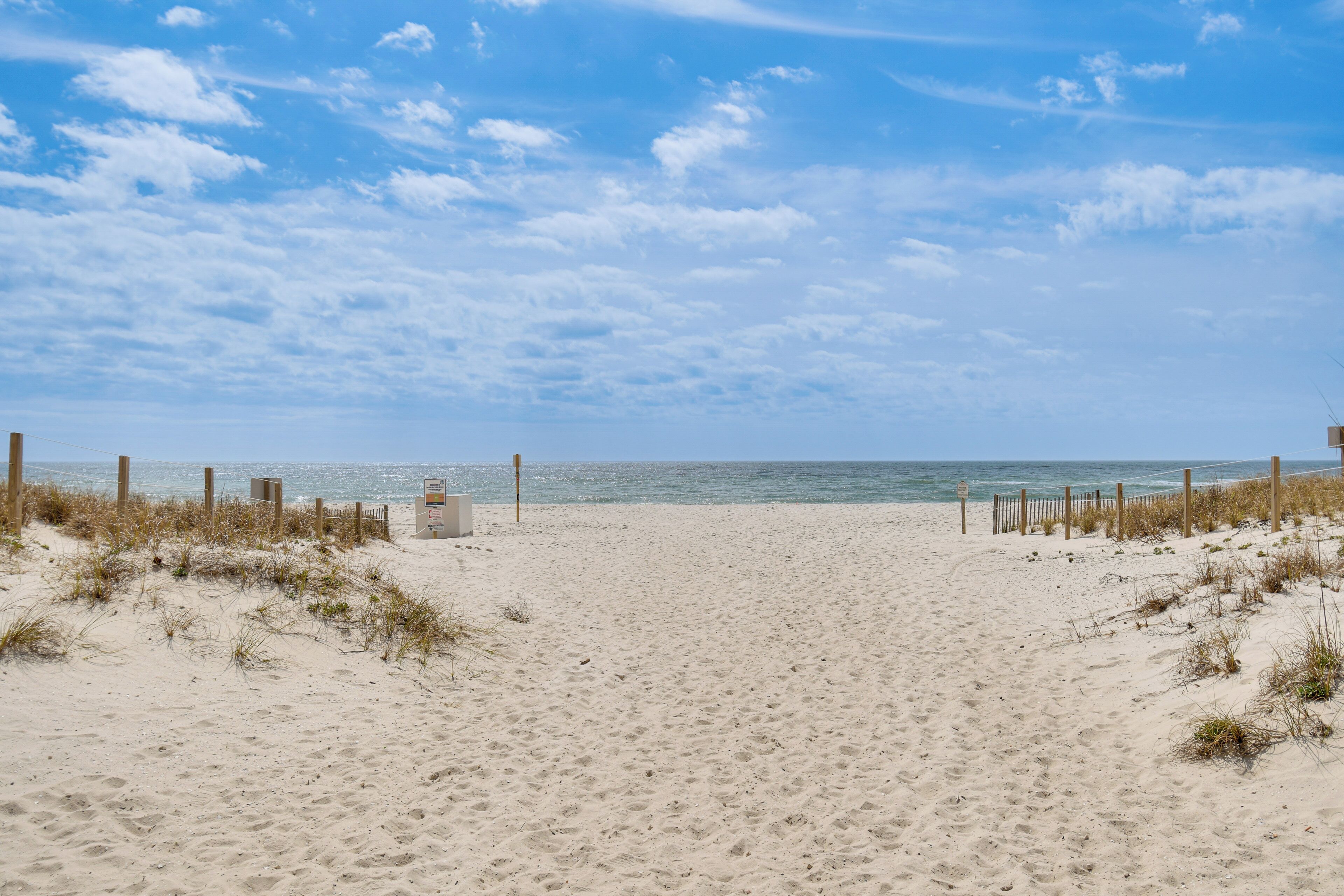 A sandy beach with a wooden fence and a signpost, leading to the ocean.