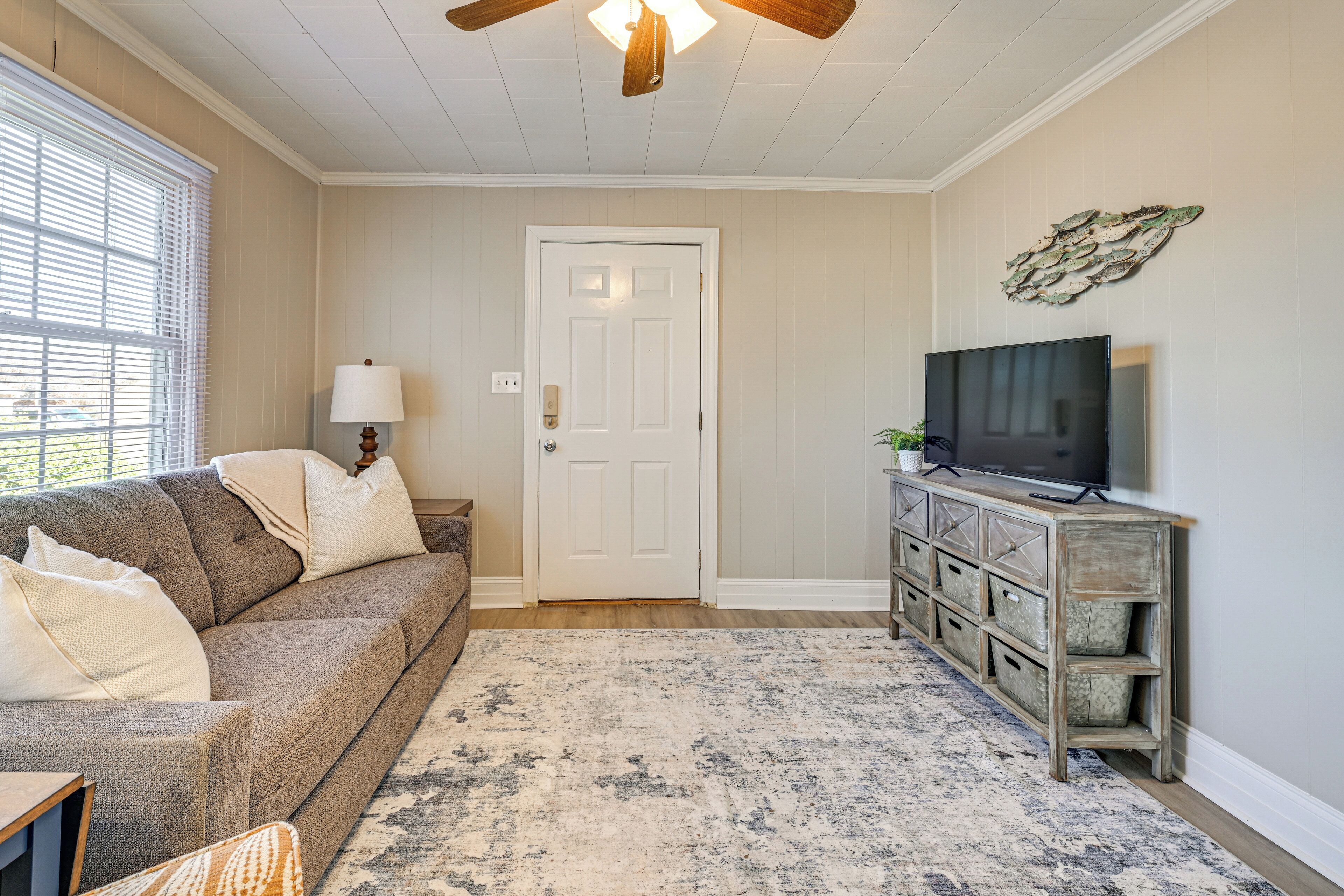 A living room with a sofa, a television on a wooden cabinet, a door, and a patterned rug.
