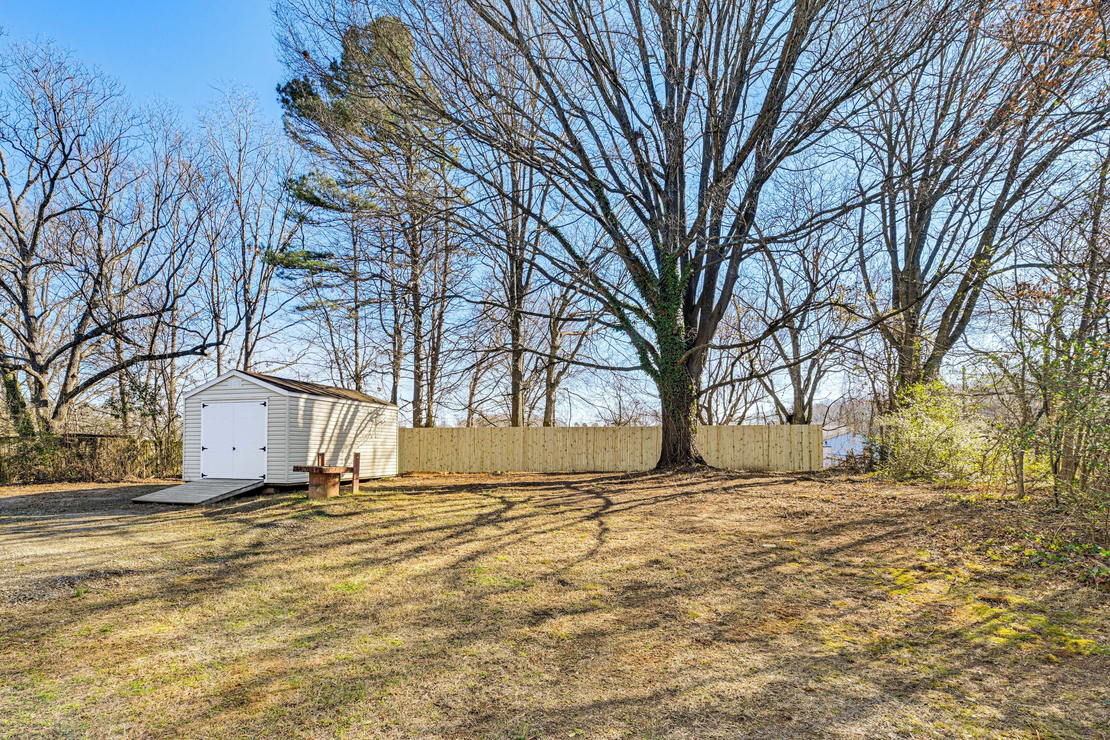 A single-story house with a detached garage, a wooden fence, and a large tree in front.