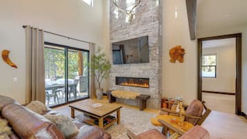 A spacious living room with a stone fireplace, leather furniture, and a large window overlooking a patio.