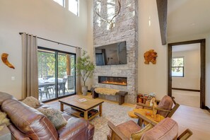 A spacious living area with a stone fireplace, leather furniture, and a large window overlooking the outdoors. - Mountain Modern and Spacious, Close to Everything! (Truckee)