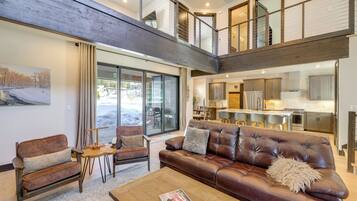 A spacious living area with a brown leather sofa, a wooden coffee table, and a painting on the wall. A staircase connects the living area to an upper level.
