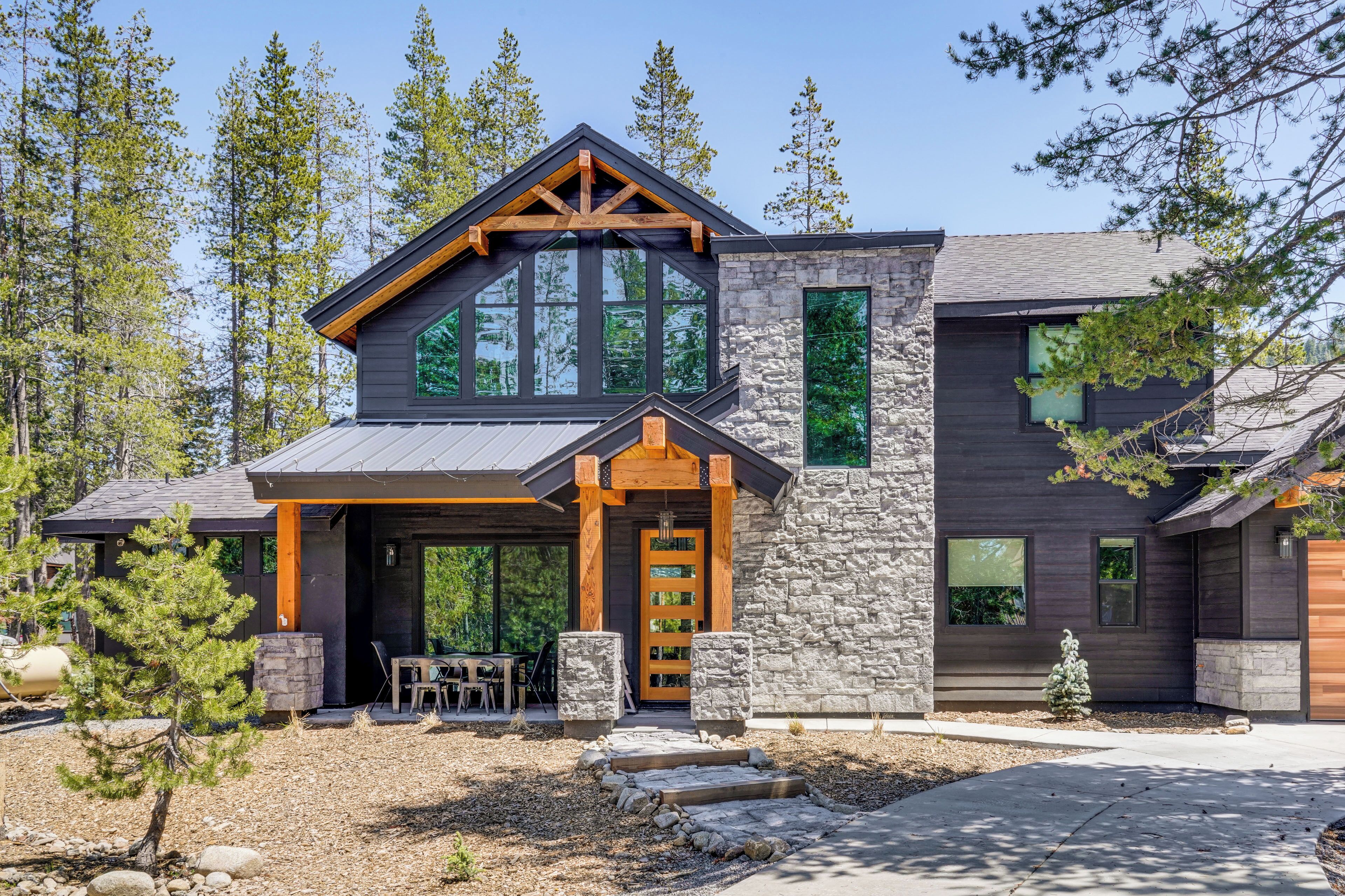 A modern house with a stone facade, large windows, and a wooden porch.