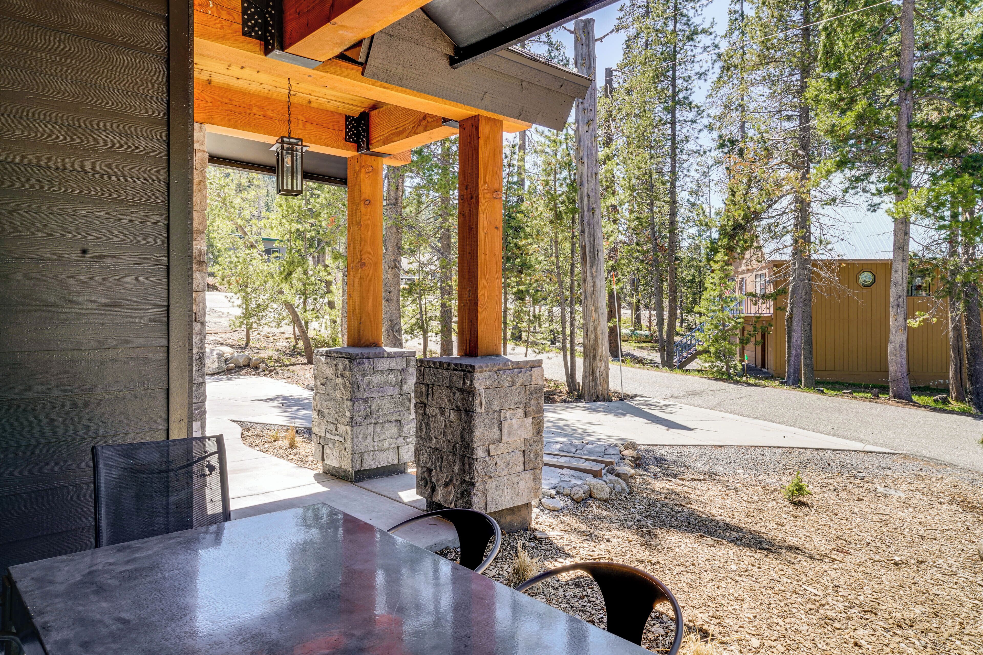 An outdoor dining area with a table and chairs, stone pillars, and a view of a forested area.