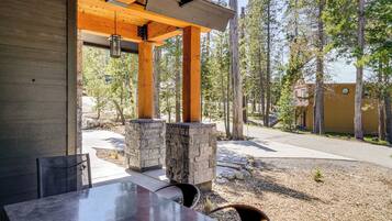 An outdoor dining area with a table and chairs, stone pillars, and a view of a forested area.