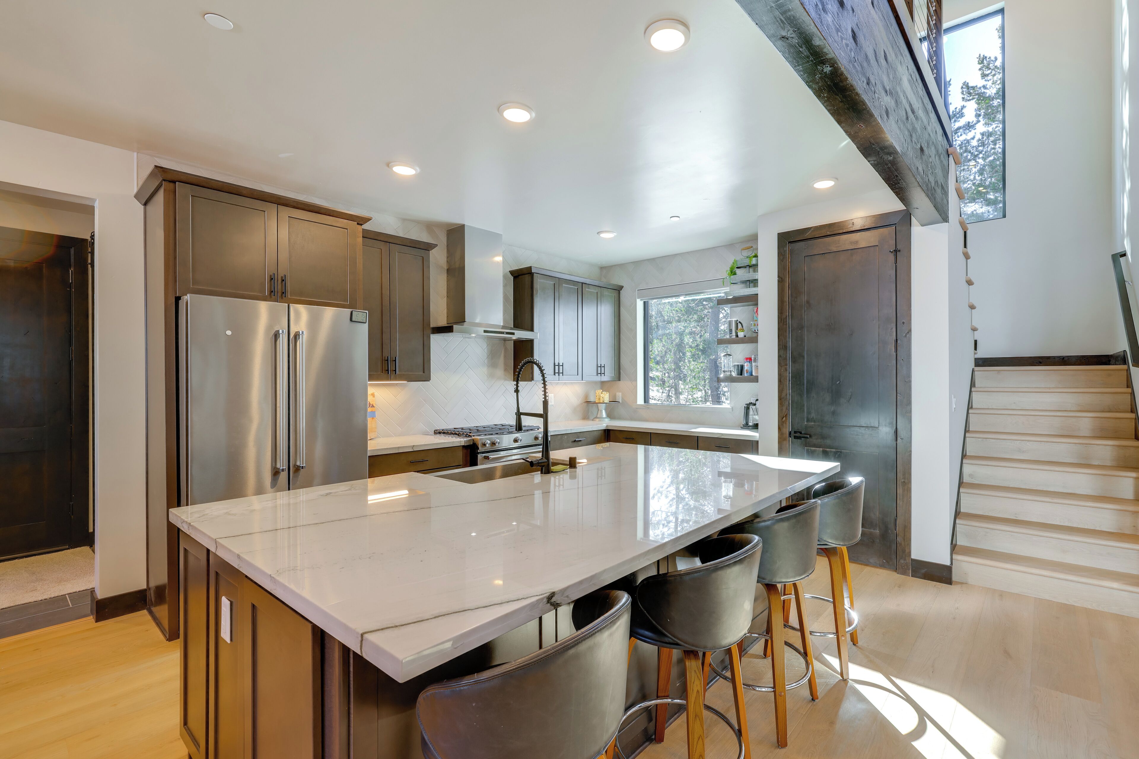 A modern kitchen with a large island, stainless steel appliances, and a view of the outdoors.