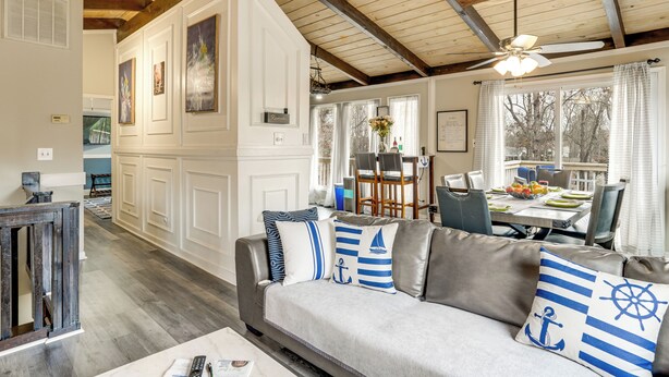 Un salon avec un canapé gris, des poutres apparentes en bois au plafond et un coin repas comprenant une table et des chaises.