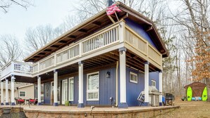 Une maison à deux étages avec un porche couvert, un garage et un petit abri où sont rangées des planches de surf.