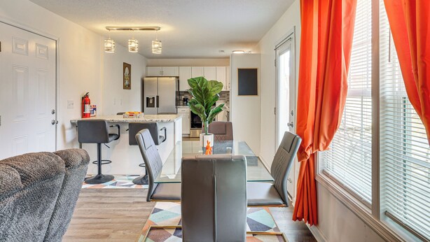 A modern kitchen with white cabinets, a dining area with a glass table, and orange curtains. - Family Home in Fountain Inn, 2 Mi to Main St! (Fountain Inn)