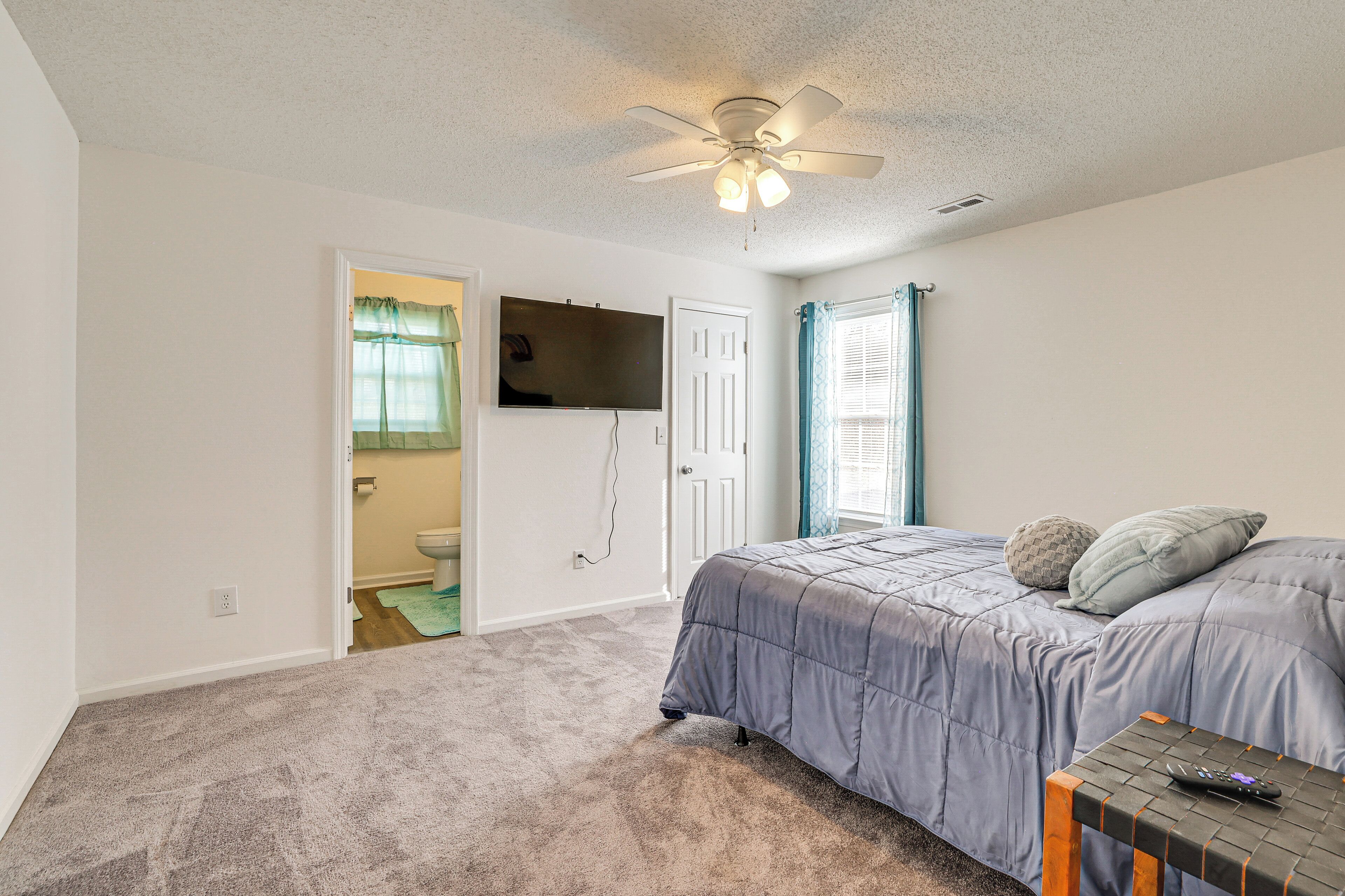 A bedroom with a bed, a ceiling fan, a TV mounted on the wall, and a door leading to a bathroom.