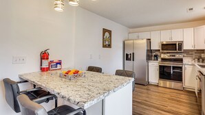 A modern kitchen with white cabinets, stainless steel appliances, and a marble countertop. There are two chairs at the island, and a fire extinguisher is visible on the wall. - Family Home in Fountain Inn, 2 Mi to Main St! (Fountain Inn)