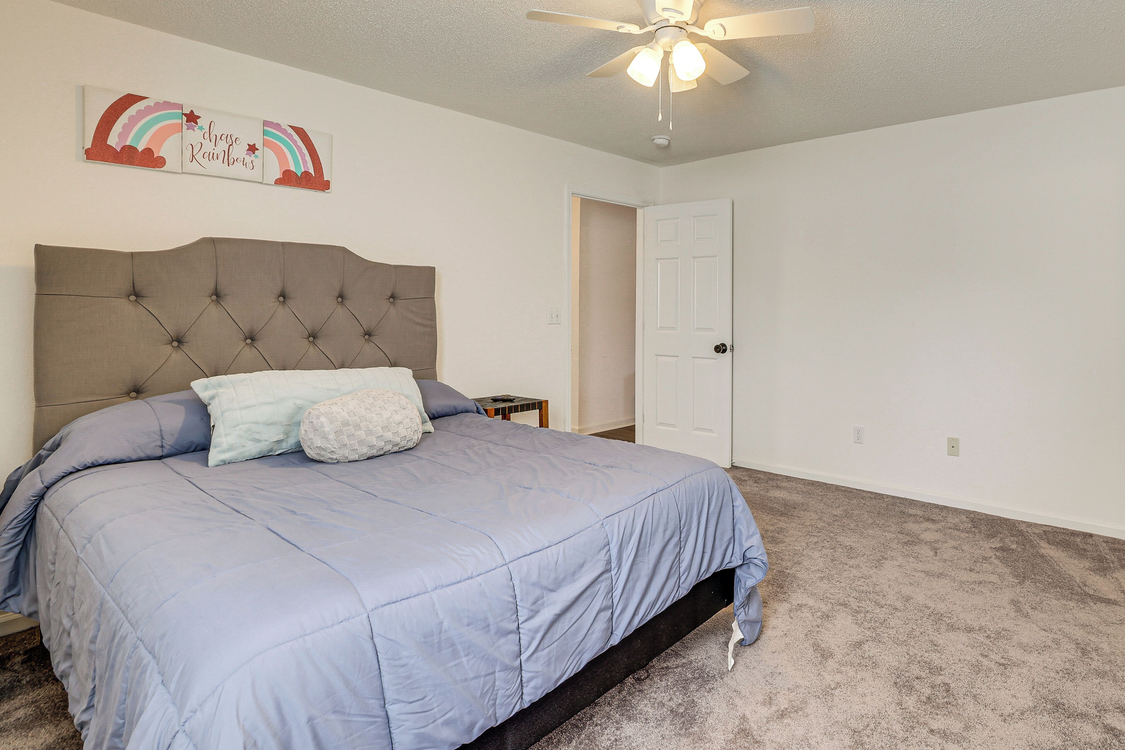 A bedroom with a tufted headboard, a blue bedspread, and a ceiling fan.