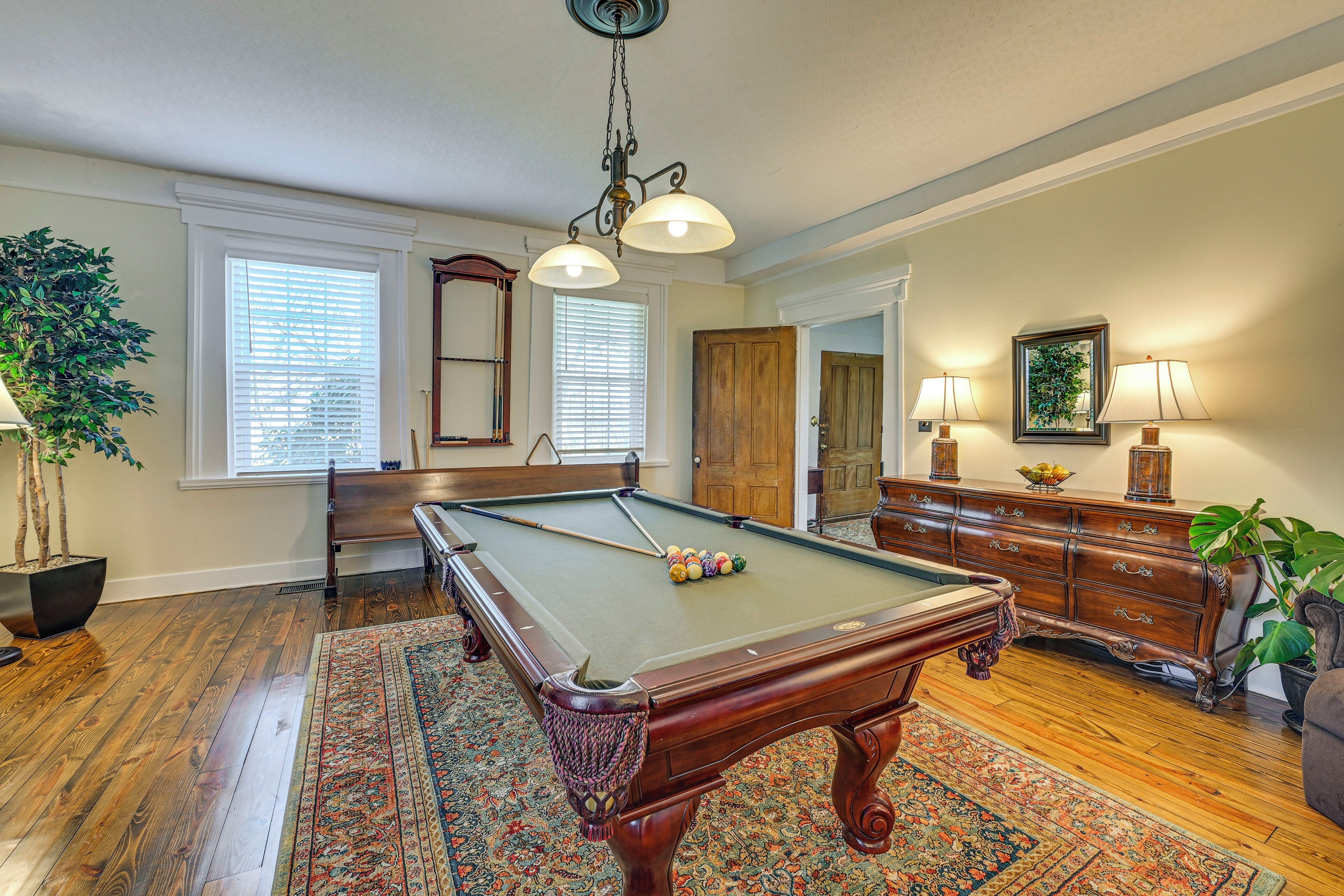 A pool table in a room with hardwood floors, a large mirror, and a wooden dresser.