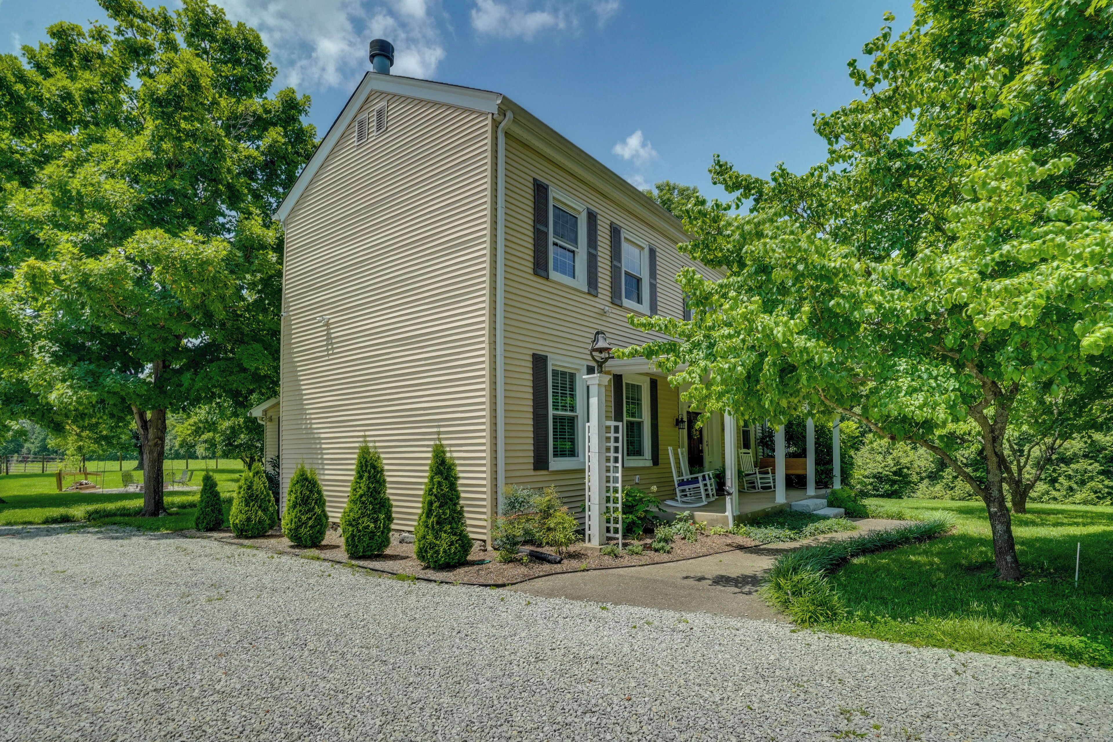 A two-story house with a front porch, a chimney, and a gravel driveway.