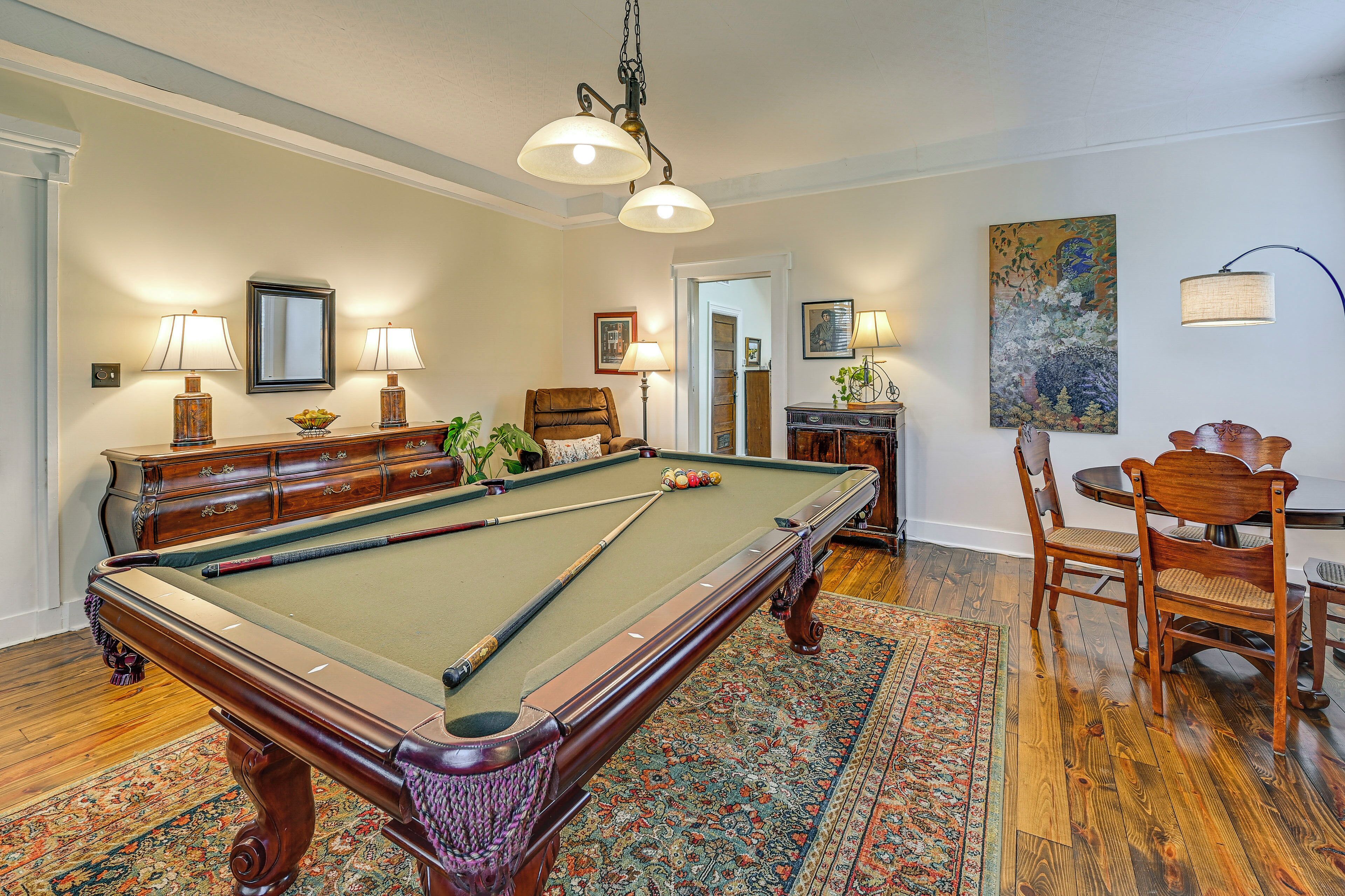 A pool table with a green felt surface, surrounded by wooden furniture and a patterned rug.