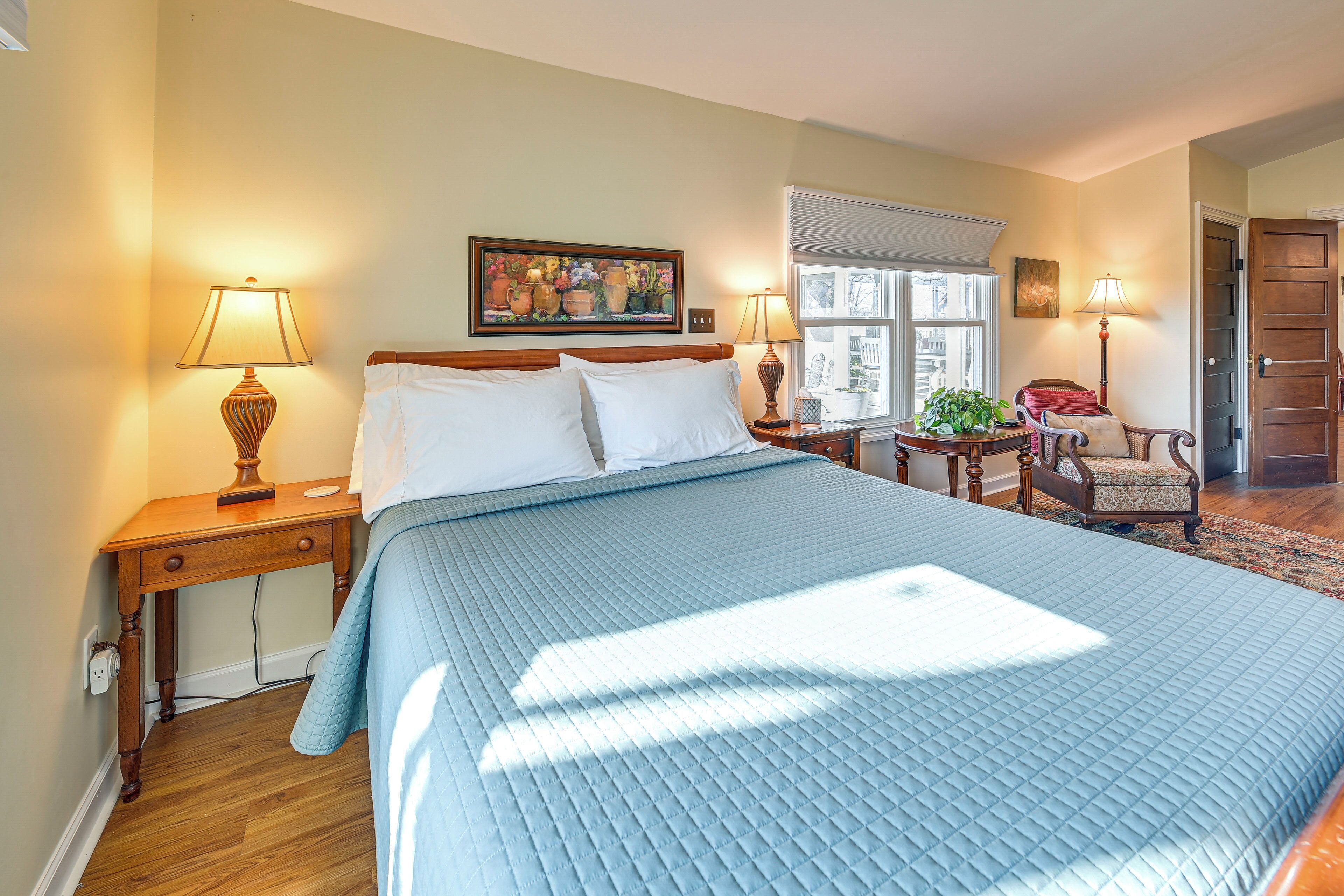 A bedroom with a large bed, two bedside tables, a chair, a window, and a door.