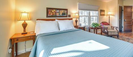 A bedroom with a large bed, two bedside tables, a chair, a window, and a door.