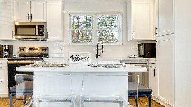 A modern kitchen with white cabinetry, a central island with two chairs, a stainless steel microwave, and a stove. - Fully Renovated! Goldsboro Gem w/ Yard & Porch (Goldsboro)