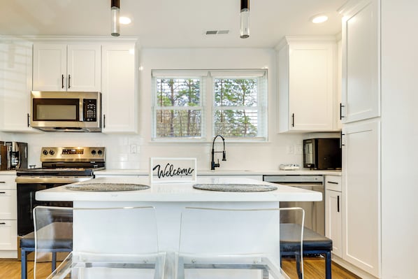 A modern kitchen with white cabinetry, a central island with bar stools, a microwave, stove, and a welcome sign. - Fully Renovated! Goldsboro Gem w/ Yard & Porch (Goldsboro)