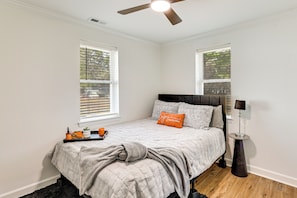 A bedroom with a bed, a ceiling fan, two windows with blinds, a bedside table with a lamp, and a tray with items on the bed. - Fully Renovated! Goldsboro Gem w/ Yard & Porch (Goldsboro)