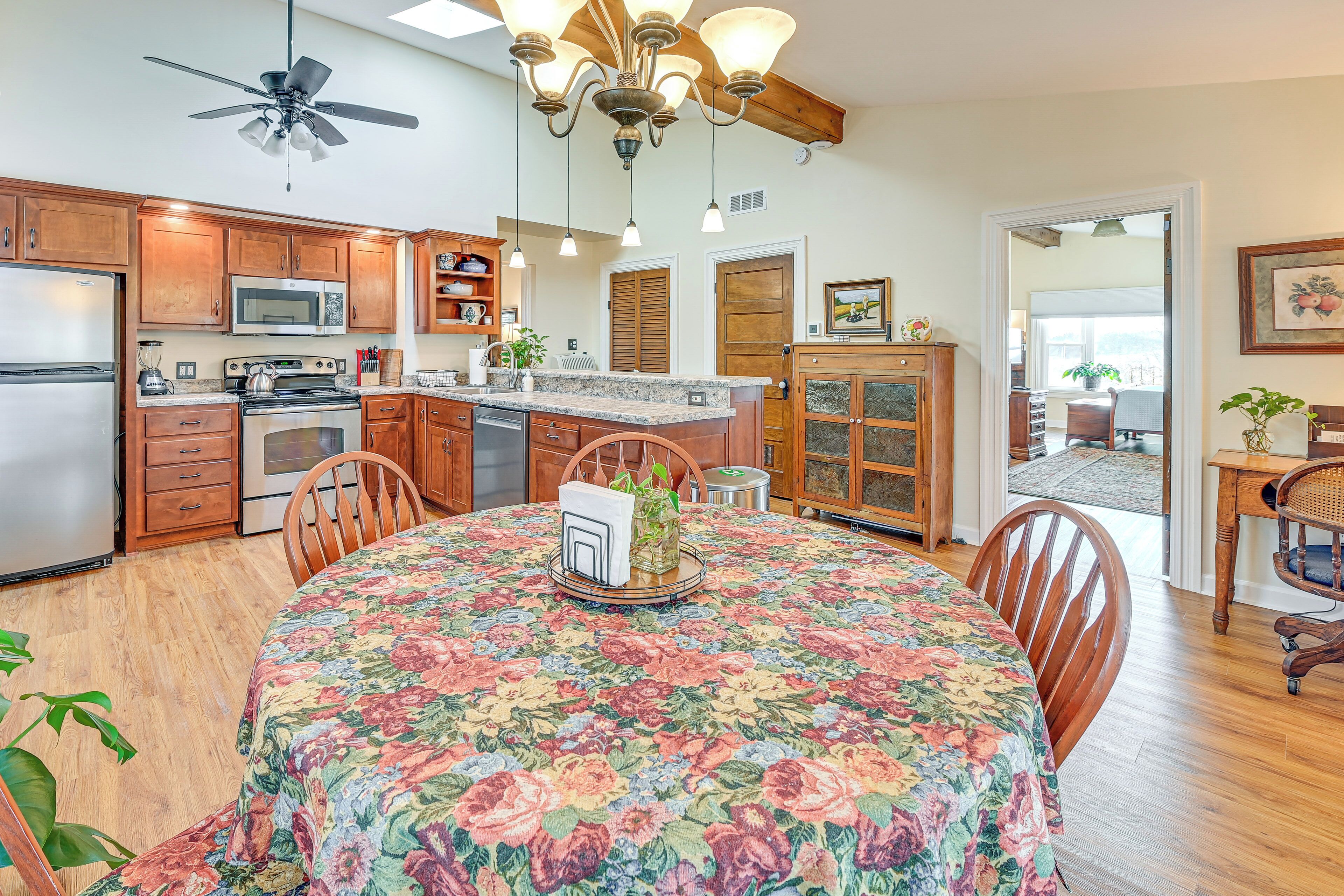 A kitchen with wooden cabinets, a microwave, stove, and a dining area with a floral tablecloth.