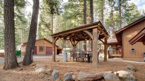 Ein rustikaler Holzpavillon mit Tisch und Stühlen, umgeben von Felsen und Kiefern.