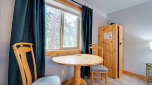 A room with a wooden table and chairs, a window with curtains, and a wooden wardrobe. - Gateway to Lassen Volcanic! Cozy Woodland Studio (Westwood)